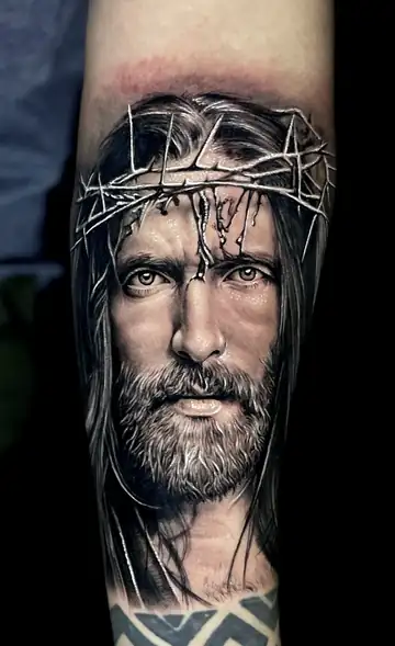 Rosto de Cristo com coroa de espinhos, tatuagem religiosa em realismo preto e cinza no antebraço